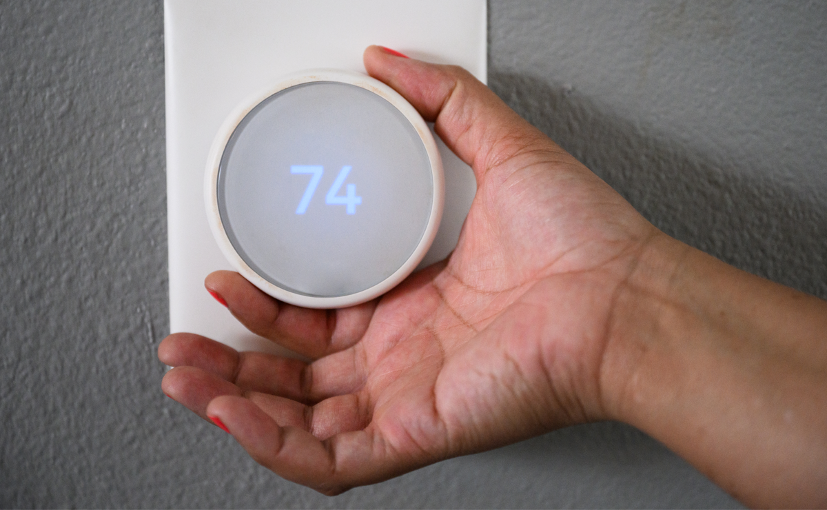 Close up of hand with nail varnish adjusting round thermostat knob against grey wall