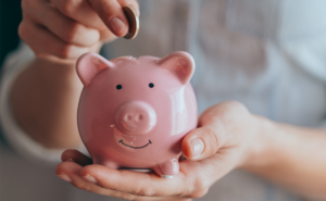 female hands hold a pink piggy bank and puts a coin - saving money on HVAC costs