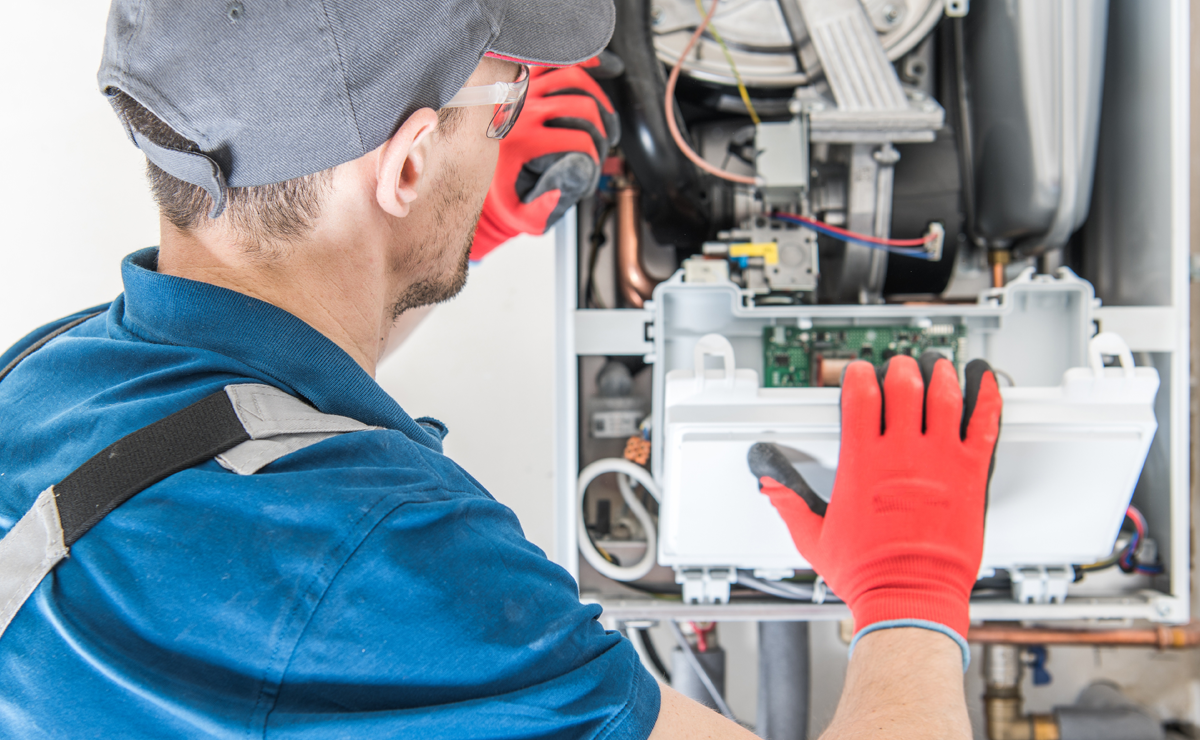 Technician performing effective furnace repair by examining and adjusting components inside a furnace unit, wearing protective gloves and a cap.