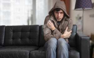 man wearing a coat sitting on a sofa shivering from cold